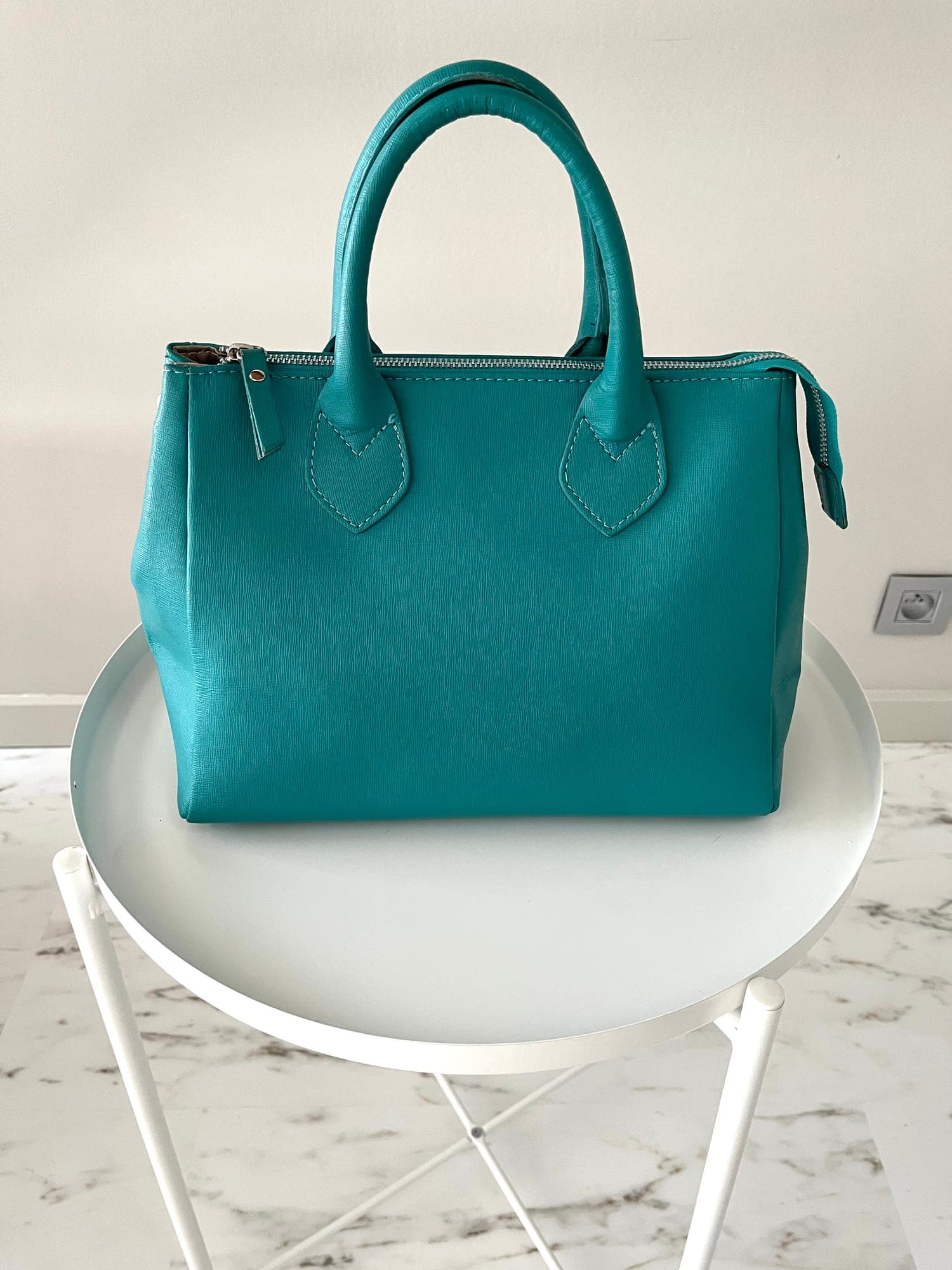 Turquoise lederen handtas met rits en hengsels en lange afneembare riem.